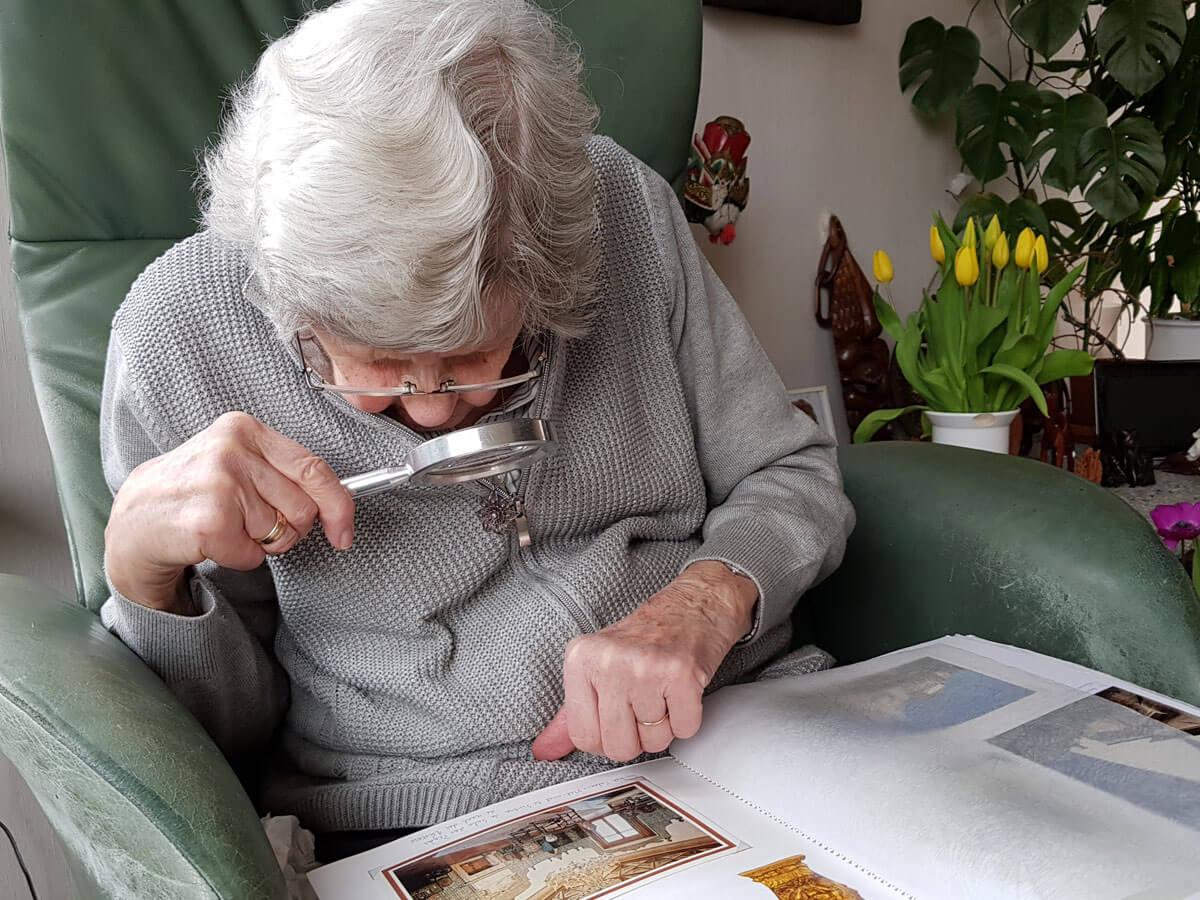 A senior woman looking through a magnifying glass is watching a photo album.